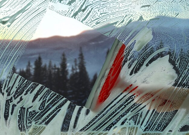 Photo femme nettoyant la fenêtre avec une raclette en gros plan vue à travers du verre transparent sur des montagnes pittoresques