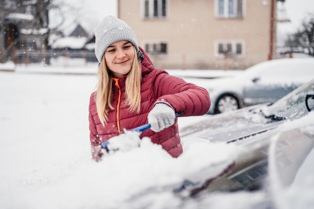 Femme nettoyant la neige de sa voiture pendant les chutes de neige en hiver Gratter la glace Nettoyage des vitres en hiver