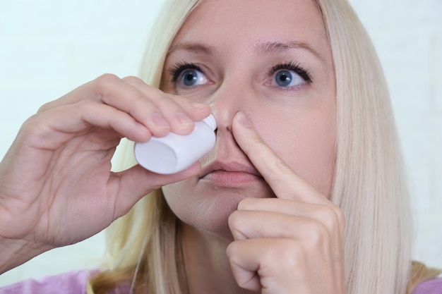 Une femme avec un nez qui coule tient un médicament dans sa main, des irrigations par pulvérisation nasale pour arrêter la rhinite allergique et la sinusite.