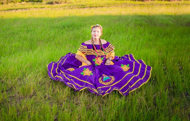 Femme nicaraguayenne en tenue folklorique traditionnelle assise sur l'herbe dans le champ Portrait de femme nicaraguayenne portant une robe folklorique nationale