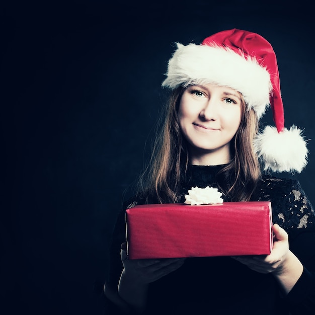 Femme de Noël en bonnet de Noel avec boîte-cadeau rouge sur fond sombre