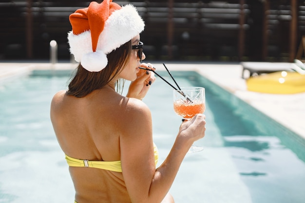 Femme De Noël Relaxante Au Bord De La Piscine. Fille Drôle Célébrant Noël Dans Une Station Balnéaire. Avec Cocktail Et Fruits.