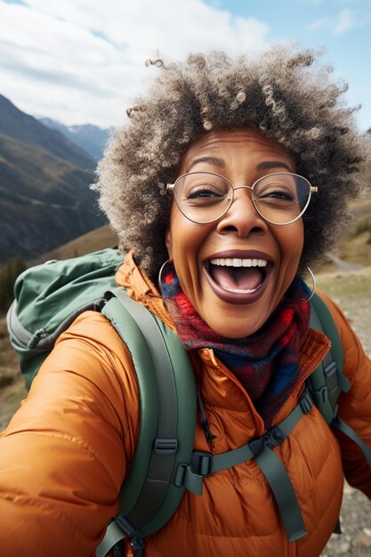 Une femme noire adulte heureuse prenant un selfie mobile au milieu du paysage pittoresque de la montagne