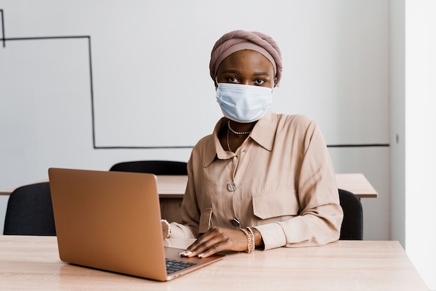 Femme noire africaine avec ordinateur portable. Utilisation de l'ordinateur pour le travail en ligne. Masque médical de protection contre le coronovirus covid-19.