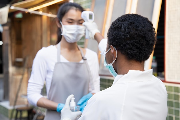 Femme noire africaine personnel de commerce de détail ou épicier vérifiant la fièvre d'un collègue asiatique par un dispositif de balayage thermique portable concept de nouvelle pratique commerciale normale