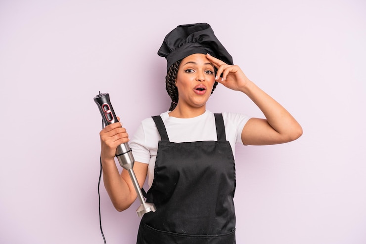 Photo femme noire afro à la recherche d'un chef étonné et surpris heureux avec un mélangeur à main