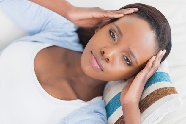 Femme noire allongée en mettant les mains sur les tempes