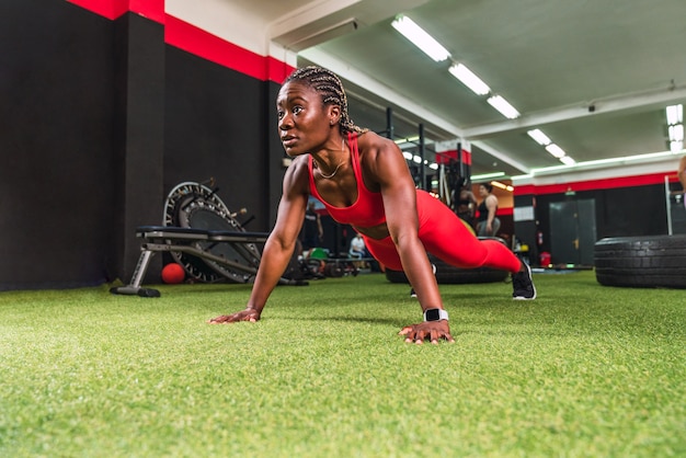 Femme noire athlétique forte dans une salle de sport faisant des exercices de pompes en vêtements de sport rouges