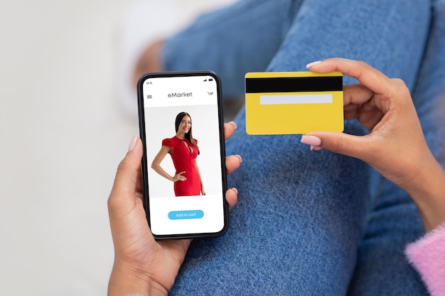 Femme noire du millénaire utilisant un téléphone moderne avec un magasin de mode à l'écran et une carte de crédit