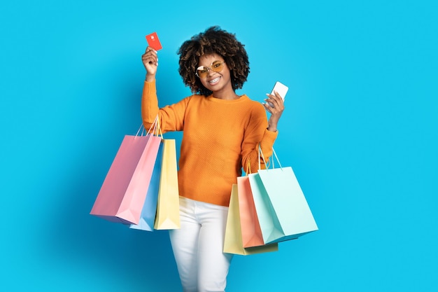 Photo femme noire élégante avec des sacs à provisions tenant une carte bancaire de téléphone