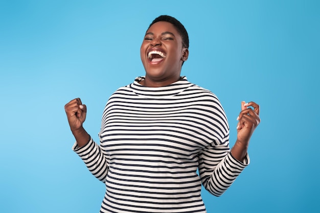 Photo femme noire émotionnelle criant gesticulant oui dans la joie fond bleu