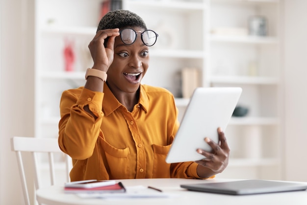 Femme noire étonnée utilisant une tablette numérique au bureau