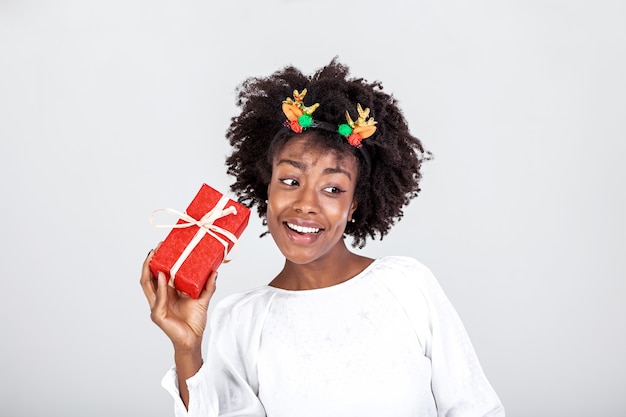 Femme noire excitée secouant la boîte-cadeau enveloppée recevant des cadeaux pour son anniversaire ou Noël debout