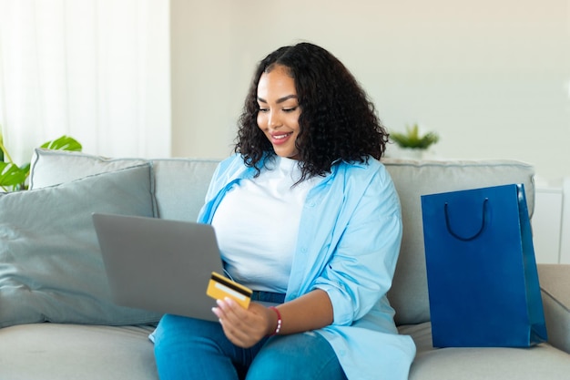 Femme noire faisant des achats en ligne à l'aide d'un ordinateur portable et d'une carte de crédit à l'intérieur