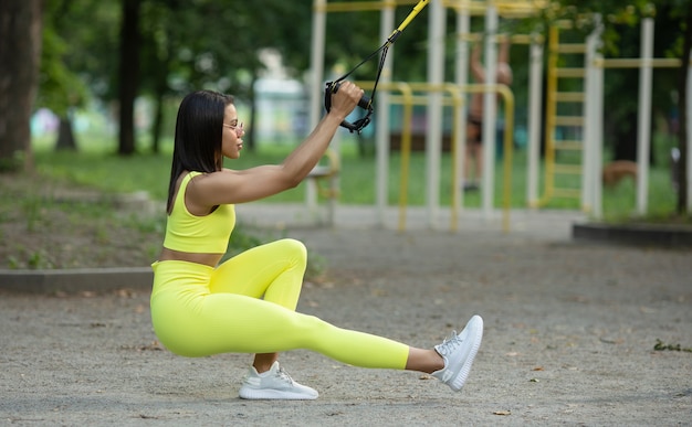 Une femme noire fait des exercices avec des ceintures de fitness TRX sur le terrain de jeu