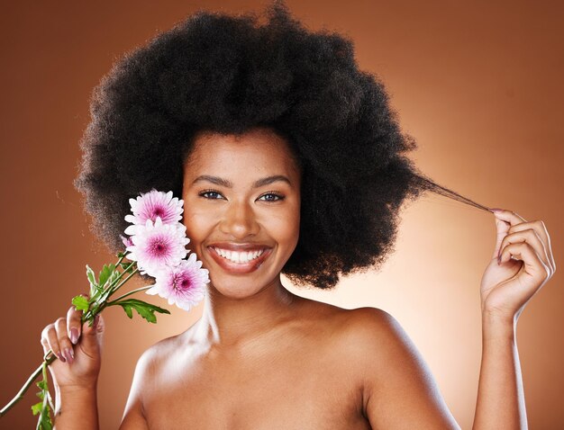 Femme noire fleurs et beauté naturelle cheveux afro et soins de la peau éclatants maquillage bio ou dermatologie écologique sur fond de studio Portrait heureux modèle africain cheveux bouclés et plantes de fleurs de marguerite rose