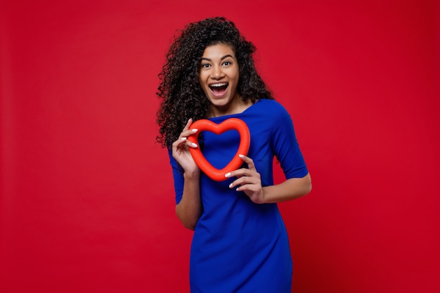 Femme noire, à, forme coeur, sourire, et, porter, robe bleue, sur, mur rouge