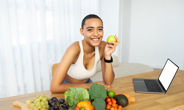 Photo femme noire joyeuse tenant une pomme verte avec une variété de fruits et légumes frais