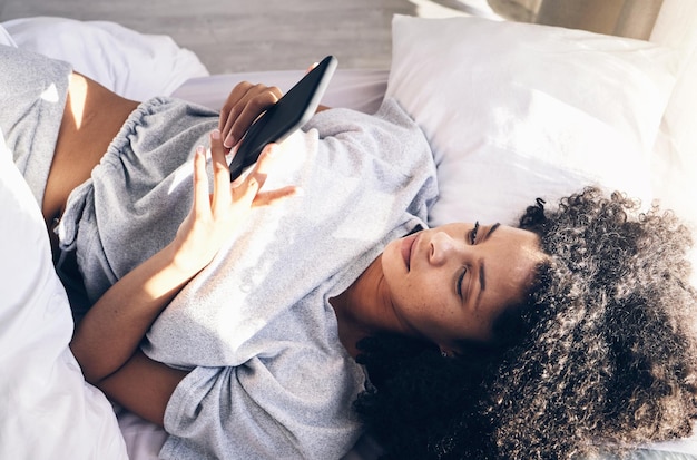 Photo femme noire lit et téléphone dans la chambre à coucher pour envoyer des sms sur les réseaux sociaux ou naviguer sur internet le matin la technologie se détend et une femme avec un smartphone mobile pour le défilement web ou la mise en réseau à la maison