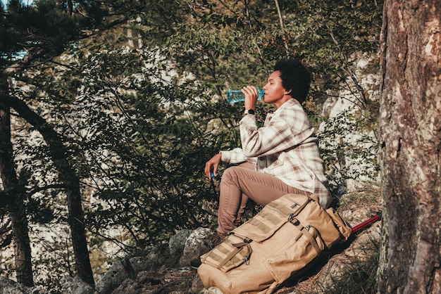 Femme noire mature prenant une pause dans l'eau lors d'une randonnée dans les montagnes.