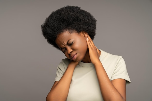 Femme noire en mauvaise santé touchant un cou douloureux souffrant d'un nerf pincé après un mouvement soudain