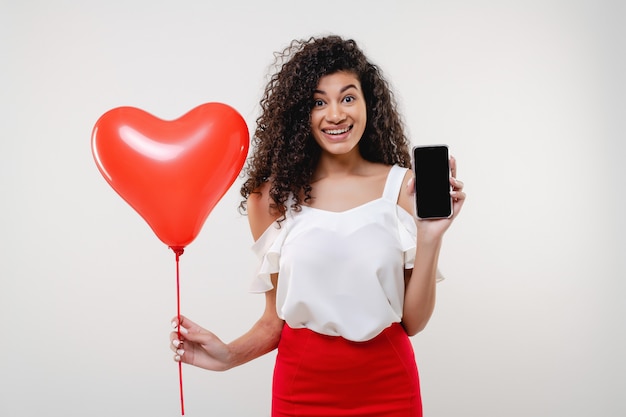 Femme noire montrant l'écran de téléphone vierge de l'espace de copie avec des ballons en forme de coeur isolé