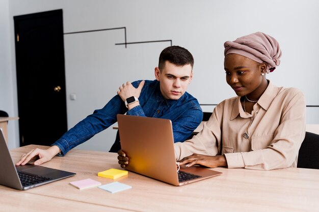 Femme noire musulmane et homme blanc avec ordinateur portable. Un couple multiethnique travaille en ligne sur un projet d'entreprise.