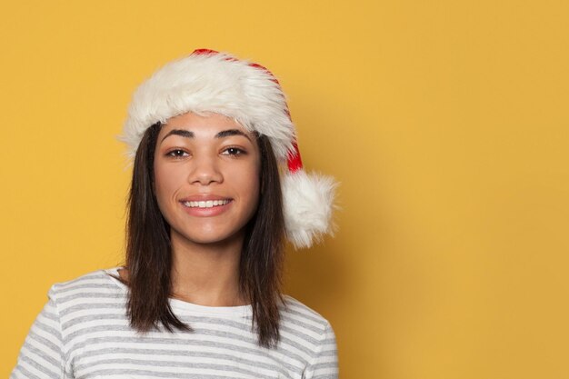 Femme noire de Noël avec un chapeau de Père Noël sur un fond jaune vif