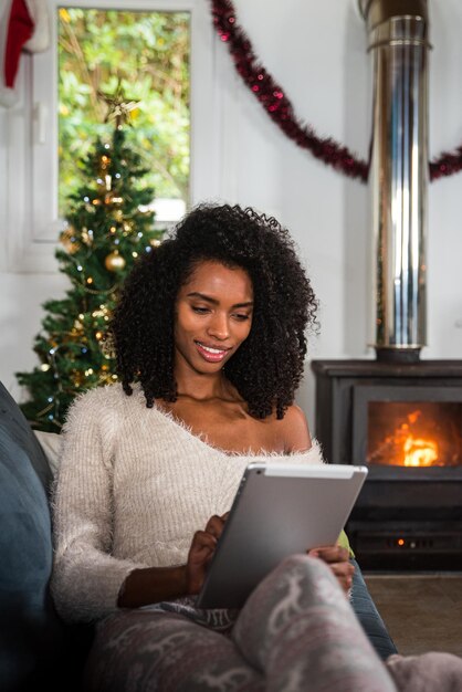 Femme noire parcourant une tablette sur un canapé