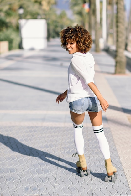 Femme noire sur patins à roulettes en promenade sur la plage avec des palmiers