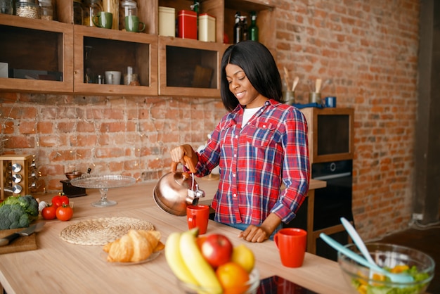 Femme noire prépare le café au petit-déjeuner dans la cuisine. Femme africaine préparant une salade de légumes à la maison