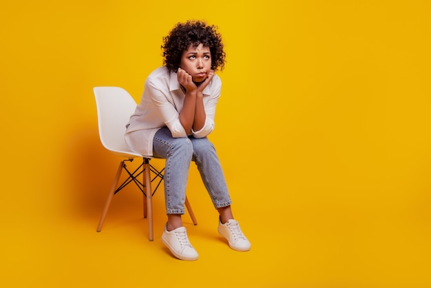 Une femme noire qui pleure a une dépression assise sur une chaise jaune sur un mur