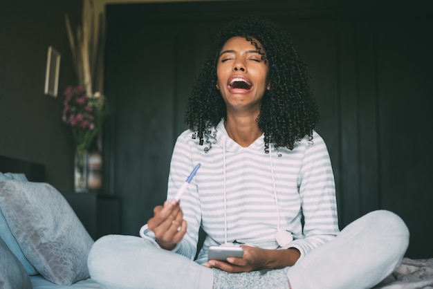 Femme noire qui pleure, triste et inquiète avec test de grossesse au lit