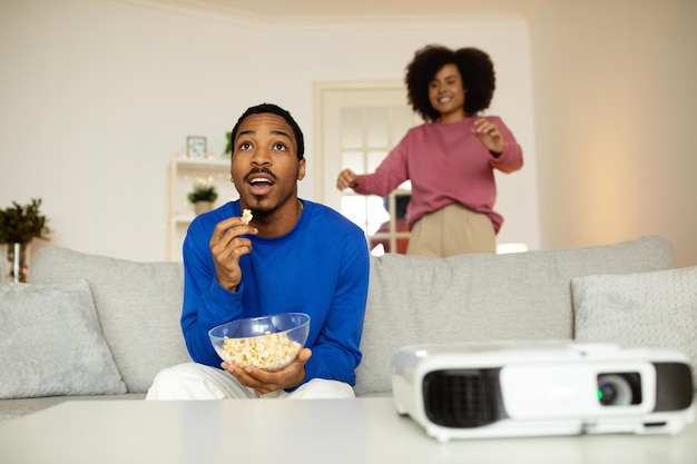 Une femme noire se moque pendant que son mari regarde un film en train de manger du pop-corn à l'intérieur