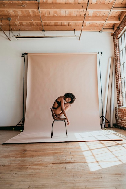 Femme noire se recroquevillant sur une chaise dans un studio