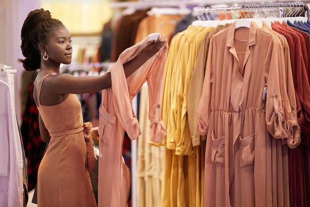 Femme noire shopping et rail de mode avec choix de vente au détail dans un magasin avec remise et offre Vêtements de centre commercial et femme africaine lors d'une vente de vêtements tenant une robe avec un client dans une boutique