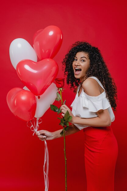 Femme noire souriante avec des ballons en forme de coeur et rose isolé