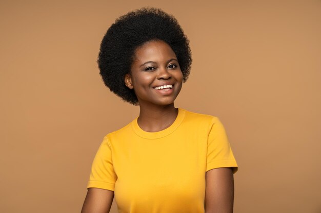 Photo femme noire souriante et joyeuse regardant la caméra isolée en chemise jaune sur fond beige