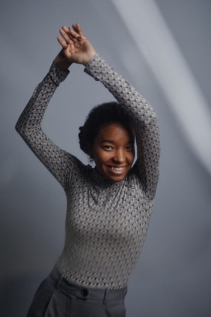 Femme noire souriante regardant la caméra et dansant sur fond gris acier