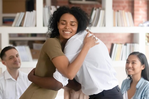 Une femme noire souriante et soulagée s'embrasse avec un ami montrant son soutien et son empathie lors d'une séance de thérapie de groupe