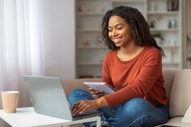 Une femme noire souriante travaillant sur un ordinateur portable à la maison pendant la journée