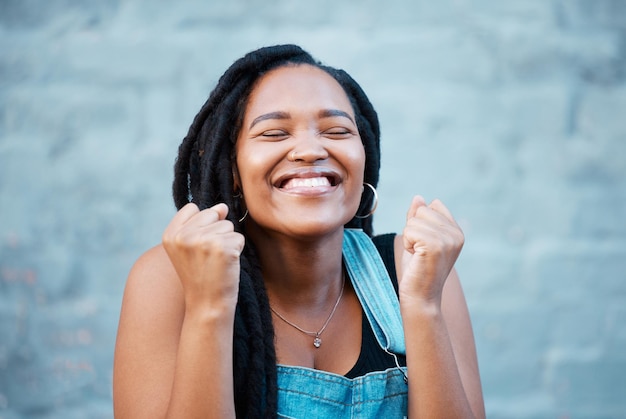 Femme noire sourire heureux et excité d'un gagnant de la Jamaïque se sentant heureux Visage souriant d'une personne avec excitation énergie positive et état d'esprit de gratitude avec un fond de briques grises