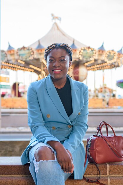 Une femme noire sourit et regarde la caméra alors qu'elle est assise avec une foire en arrière-plan