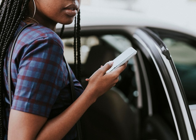 Femme noire tenant son téléphone en montant dans une voiture