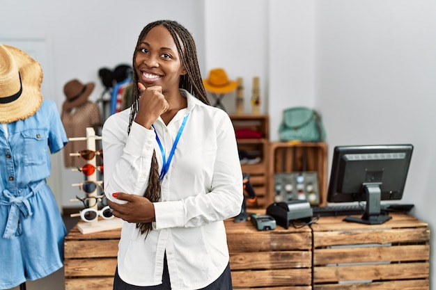 Photo femme noire avec des tresses travaillant comme gestionnaire dans une boutique de vente au détail, confiante devant la caméra, souriante avec les bras croisés et la main levée sur le menton. penser positivement.