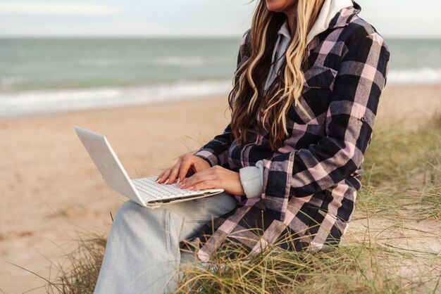 Femme nomade méconnaissable travaillant à distance sur un ordinateur portable sur la plageConcept de voyage et de style de vie nomade