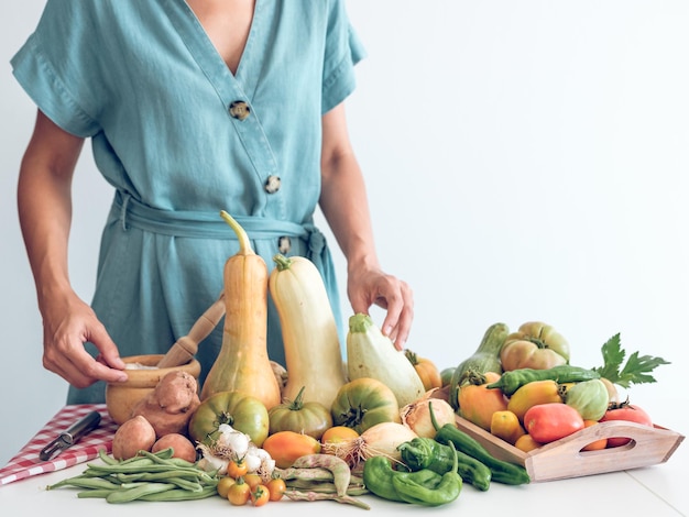 Femme non reconnaissable de la culture démontrant des légumes frais mûrs assortis, y compris des citrouilles et des tomates avec du poivre placés dans un plateau en bois sur table sur un fond blanc