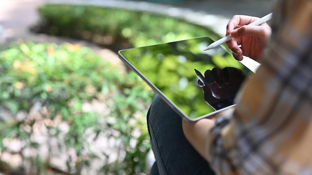 Une femme notant ses idées de projet sur le pavé tactile de sa tablette tout en se relaxant dans le parc