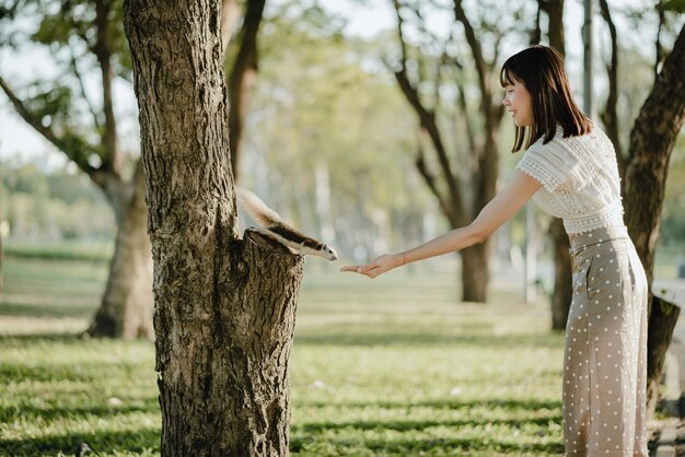 Photo une femme nourrit un écureuil debout près du tronc d'un arbre