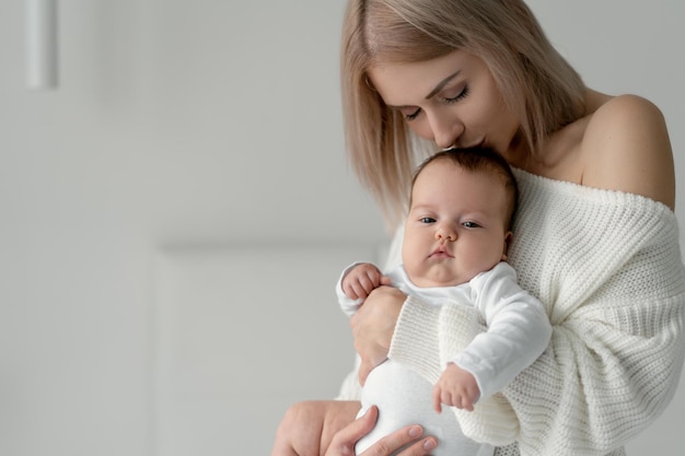 Une femme avec un nouveau-né dans les bras embrasse la tête de sa fille. Vêtements en coton blanc de qualité. Place pour votre texte. Espace de copie.